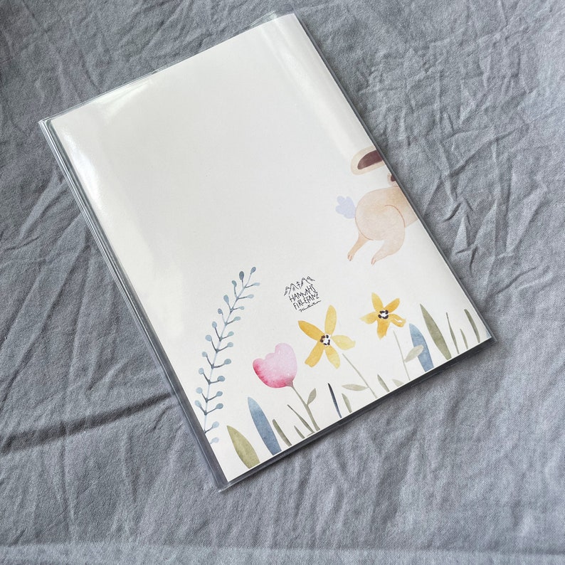 May include: A white card with a watercolor illustration of a bunny rabbit hopping over a field of flowers. The flowers are yellow, pink, and blue. The text "Mama Happy Birthday" is written on the card.