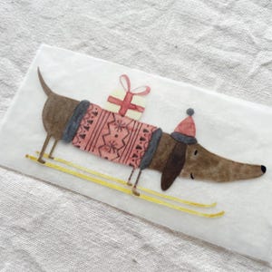 May include: A brown dachshund wearing a red and grey sweater and a red hat is carrying a wrapped gift on its back. The dachshund is on skis with yellow poles.