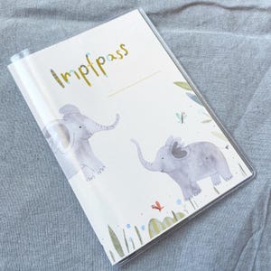 May include: A white vaccination passport with the word "Impfpass" in gold lettering. The cover features two illustrated elephants and butterflies in a watercolour style.