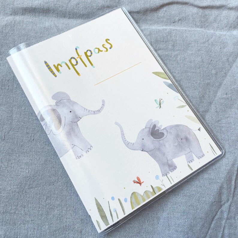 May include: A white vaccination passport with the word "Impfpass" in gold lettering. The cover features two illustrated elephants and butterflies in a watercolour style.