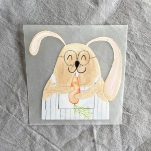 May include: A watercolor illustration of a brown bunny wearing glasses and a blue and white striped apron, holding a carrot in its paws.