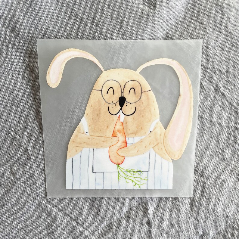 May include: A watercolor illustration of a brown bunny wearing glasses and a blue and white striped apron, holding a carrot in its paws.