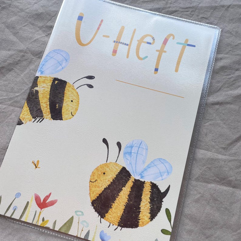 May include: A protective cover for a medical booklet featuring the text U-Heft in tan lettering with colorful accents. The design includes two illustrated bumblebees with yellow and black stripes and light blue wings, set against a cream background.