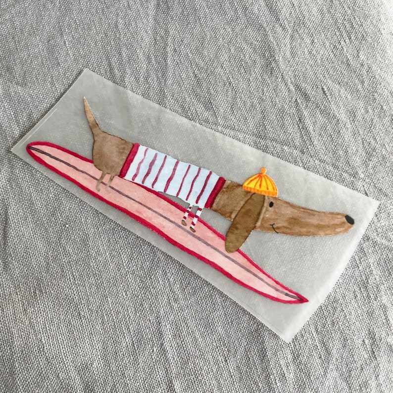 May include: A brown dachshund wearing a red and white striped shirt and a yellow hat is riding a pink surfboard.