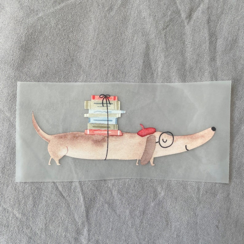 May include: A brown dachshund with a red beret and glasses is carrying a stack of books tied with a black ribbon.