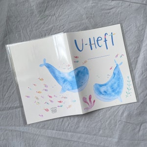 Może przedstawiać: Ilustracja niebieskiego i białego wieloryba na białym tle z tekstem "U-Heft" u g&oacute;ry strony. Ilustracja jest otoczona małymi kolorowymi rybami.