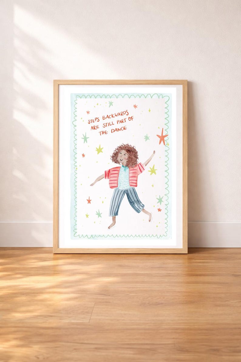 May include: A framed art print featuring a whimsical illustration of a person dancing. The person is wearing a pink striped jacket, blue striped pants, and a blue shirt. The text "Steps Backwards Are Still Part of the Dance" is written above the person, surrounded by stars.