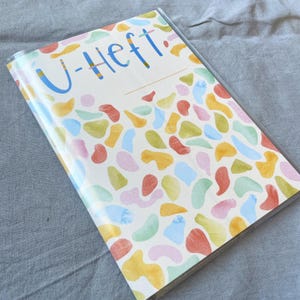 May include: A white binder with a colorful abstract pattern and the text "U-Heft" in blue.
