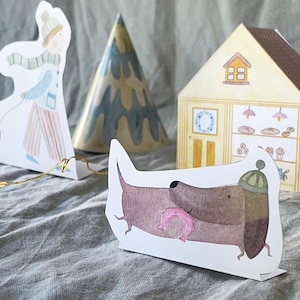 May include: A set of paper cutouts featuring a snowman, a person pulling a sled, a Christmas tree, a house with a bakery inside, and a dachshund wearing a hat and holding a pink donut.
