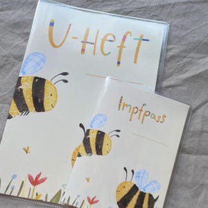 May include: Two protective covers for documents, one labeled U-Heft and the other Impfpass. Both feature a cream background with illustrations of yellow and black striped bees, blue wings, and small colorful flowers at the bottom edge.