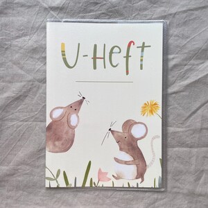 May include: A rectangular booklet cover with a cream background featuring the text U-Heft in green letters. The illustration shows two brown mice, a yellow dandelion, and a small pink flower, all enclosed in a clear protective plastic sleeve.