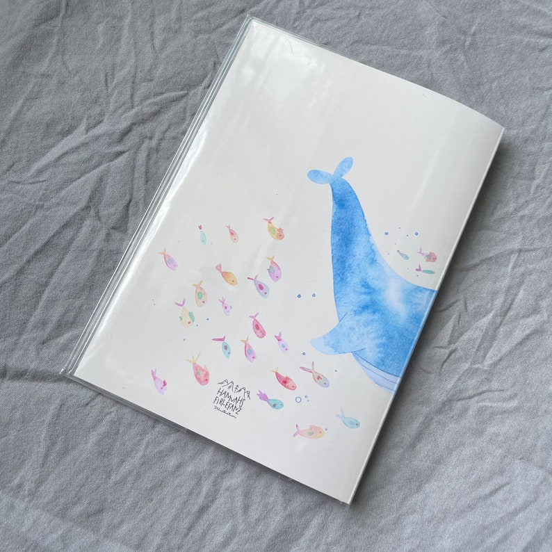 Może przedstawiać: Aquarela przedstawiająca niebieskiego wieloryba otoczonego ławicą kolorowych ryb. W lewym dolnym rogu nadrukowany jest tekst "BATMAN HANNAH FIREFLY".