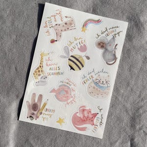 K&ouml;nnte beinhalten: Ein Stickerbogen mit Aquarellillustrationen von Tieren und inspirierenden S&auml;tzen auf Deutsch. Designs umfassen eine Giraffe, eine Biene, eine Katze, einen Fuchs und eine Maus, mit Texten wie "Ich bin mutig" und "Ich werde geliebt!"