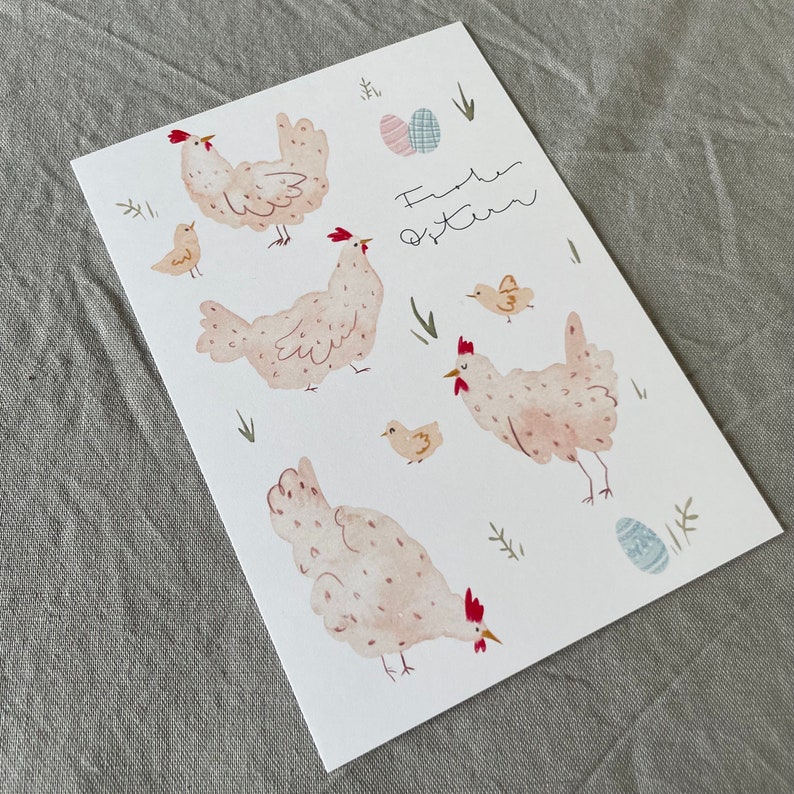 Pu&ograve; includere: Un biglietto bianco con un'illustrazione ad acquerello di galline e pulcini. Il biglietto ha il testo "Frohe Ostern" scritto su di esso, che in tedesco significa "Buona Pasqua".