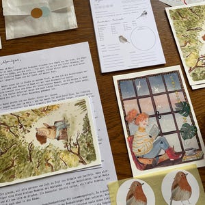 Op de afbeelding: Een verzameling ge&iuml;llustreerde briefpapierartikelen, waaronder ansichtkaarten, stickers en een notitieblok met vogelillustraties. Het kunstwerk toont een gezellige sc&egrave;ne van een persoon die bij een raam leest en een aquarel van een vogel.