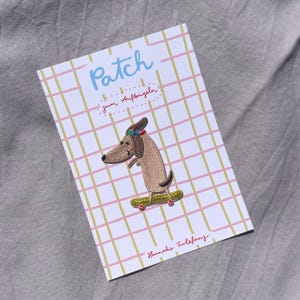 May include: Embroidered patch featuring a dachshund dog on a skateboard. The patch is on a card with the word "Patch" in blue, and text in German. The card has a pink and yellow grid pattern, with the name "Hannahs Friefanz" in red.