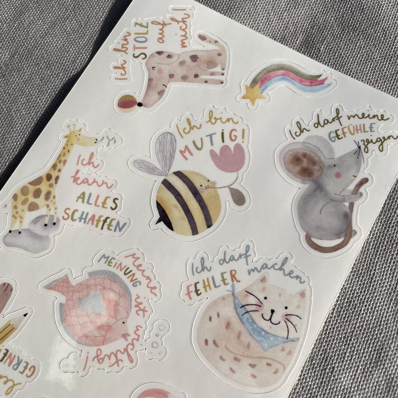 K&ouml;nnte beinhalten: Ein Bogen mit Aufklebern mit Aquarellillustrationen von Tieren und motivierenden S&auml;tzen. Die Aufkleber zeigen eine Giraffe, eine Biene, eine Maus, eine Katze und einen Hund, jeweils mit einem einzigartigen Design und einer Sprechblase.