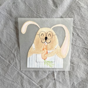 Peut inclure: Une illustration aquarelle d'un lapin brun portant des lunettes et un tablier rayé, tenant une carotte dans ses pattes.