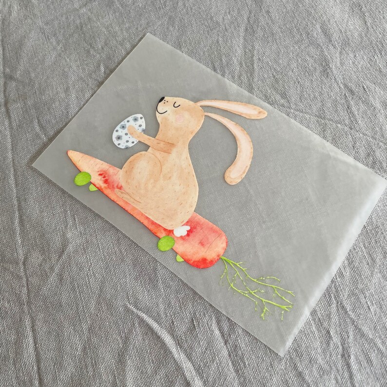 May include: A brown bunny rabbit with a white egg in its paws is riding a carrot-shaped skateboard with green wheels. The carrot has green leaves.