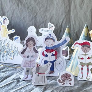May include: A set of paper Christmas characters, including a reindeer, a snowman, a Christmas tree, a dog, and people singing carols. The characters are all cut out and ready to be used for a Christmas craft project.
