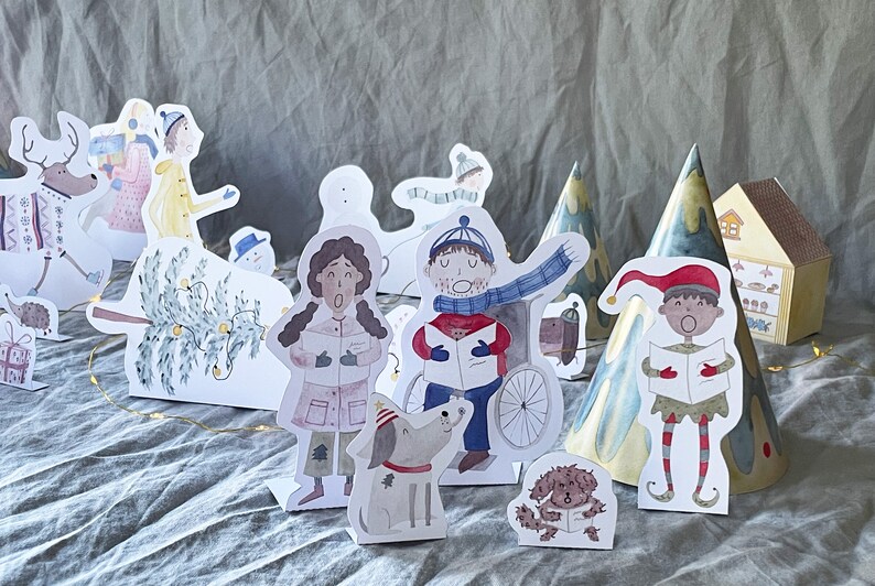 May include: A set of paper Christmas characters, including a reindeer, a snowman, a Christmas tree, a dog, and people singing carols. The characters are all cut out and ready to be used for a Christmas craft project.