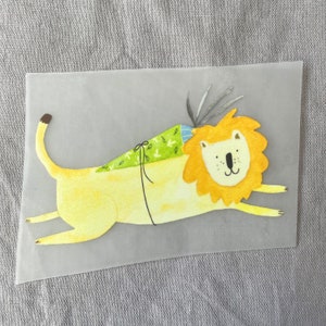 May include: A yellow lion with a green and blue patterned scarf is lying on its side with its head turned to the right. The lion has a friendly expression and a black nose.