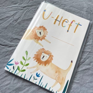 K&ouml;nnte beinhalten: Ein wei&szlig;es Notizbuch mit einem bunten Design mit zwei L&ouml;wen und dem Text "U-Heft".