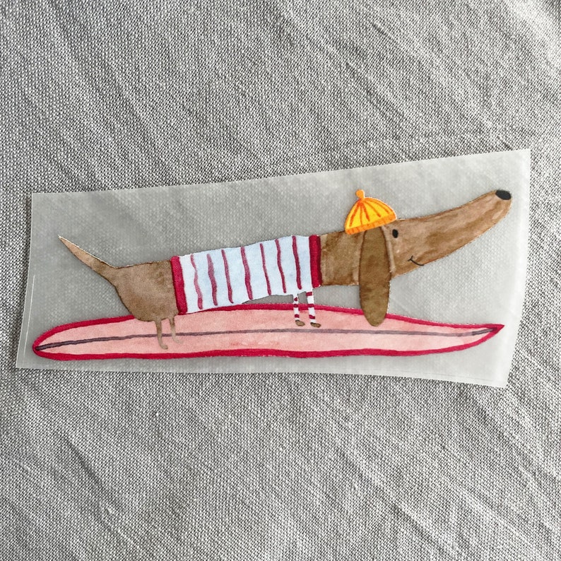 May include: A brown and white dachshund wearing a yellow hat and red and white striped shirt is riding a pink surfboard.