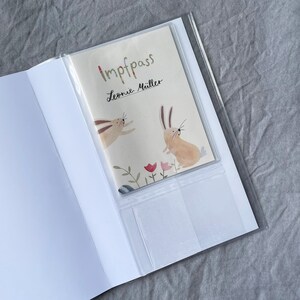 May include: A white booklet with a clear plastic cover. The cover has a colorful illustration of two rabbits and the text "Impfpass Leonie M&uuml;ller".