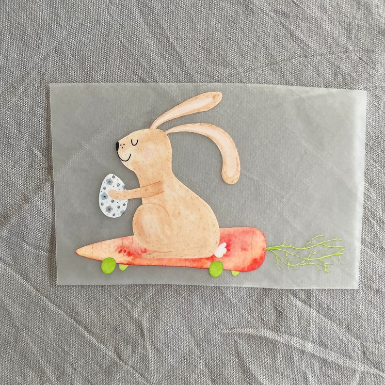 May include: A brown bunny rabbit with a white egg in its paw is riding a red carrot skateboard with green wheels. The bunny is smiling and has a white tail.