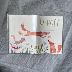 Może przedstawiać: Otwarty notatnik z fantazyjną ilustracją lisa, wiewi&oacute;rki i liści. Lis jest przedstawiony w trakcie skoku, z tekstem "U-Heft" na g&oacute;rze. Grafika ma kolorowy, akwarelowy styl z zabawnym motywem inspirowanym naturą.
