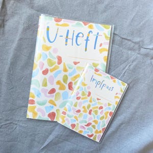 May include: Two clear plastic covered notebooks with colorful abstract patterns. The larger notebook has the text "U-Heft" on the front. The smaller notebook has the text "Impfpass" on the front.