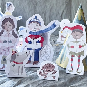 May include: A set of paper cutouts featuring a Christmas scene with a snowman, a dog, a person in a wheelchair, a person in a elf costume, and a tree. The cutouts are all white with watercolor illustrations.