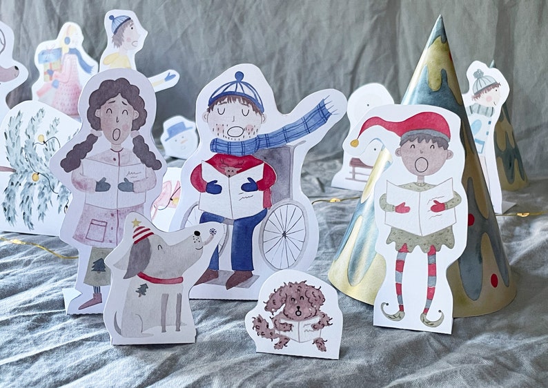May include: A set of paper cutouts featuring a Christmas scene with a snowman, a dog, a person in a wheelchair, a person in a elf costume, and a tree. The cutouts are all white with watercolor illustrations.