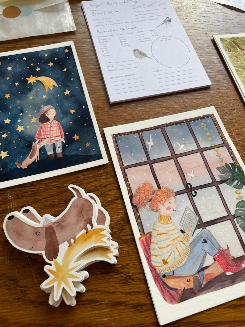 Op de afbeelding: Een verzameling aquarel illustraties en stickers met grillige sc&egrave;nes. E&eacute;n illustratie toont een kind en een hond onder een sterrenhemel. Een andere toont een persoon die bij een raam leest. Er is ook een notitieblok met vogel illustraties.