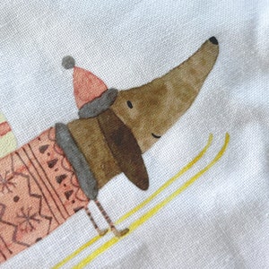 May include: A brown and white dachshund wearing a pink and white sweater and a red hat is skiing down a snowy hill. The dachshund is smiling and has a happy expression on its face.