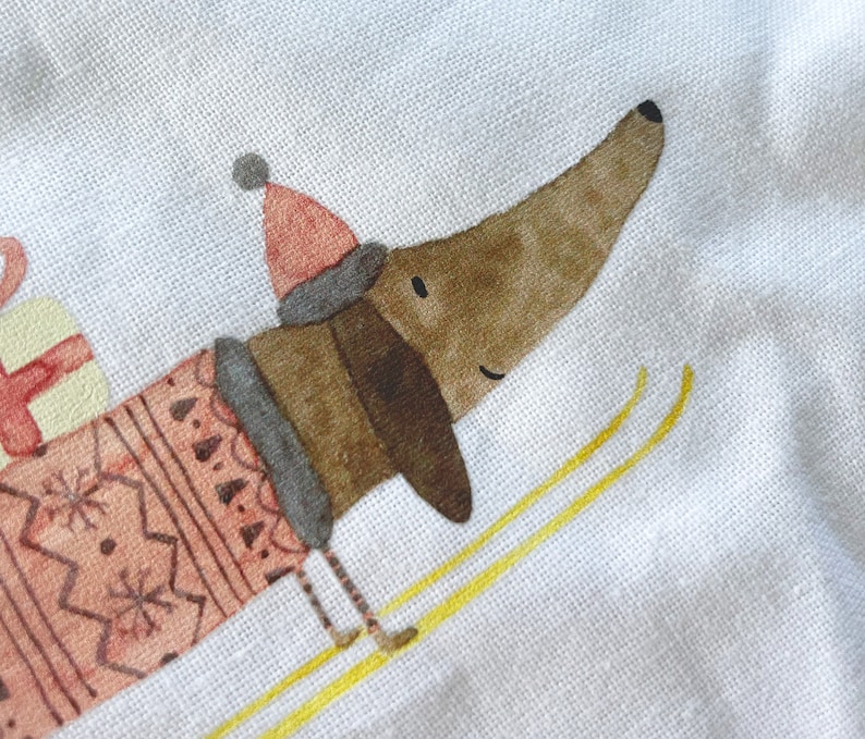 May include: A brown and white dachshund wearing a pink and white sweater and a red hat is skiing down a snowy hill. The dachshund is smiling and has a happy expression on its face.