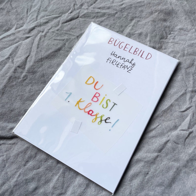 Może przedstawiać: Biała kartka z nadrukowanym tekstem "B&uuml;gelbild Hannahs Firlefanz Du bist 1. Klasse!". Kartka znajduje się w przezroczystej plastikowej osłonie.