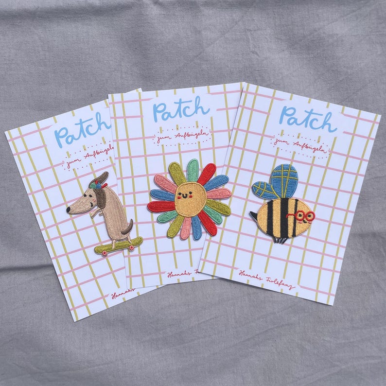 May include: Three embroidered patches on cards. One features a dachshund on a skateboard, another a smiling flower, and the third a bee wearing glasses. Each card has the word "Patch" and the text "zum Aufb&uuml;geln".