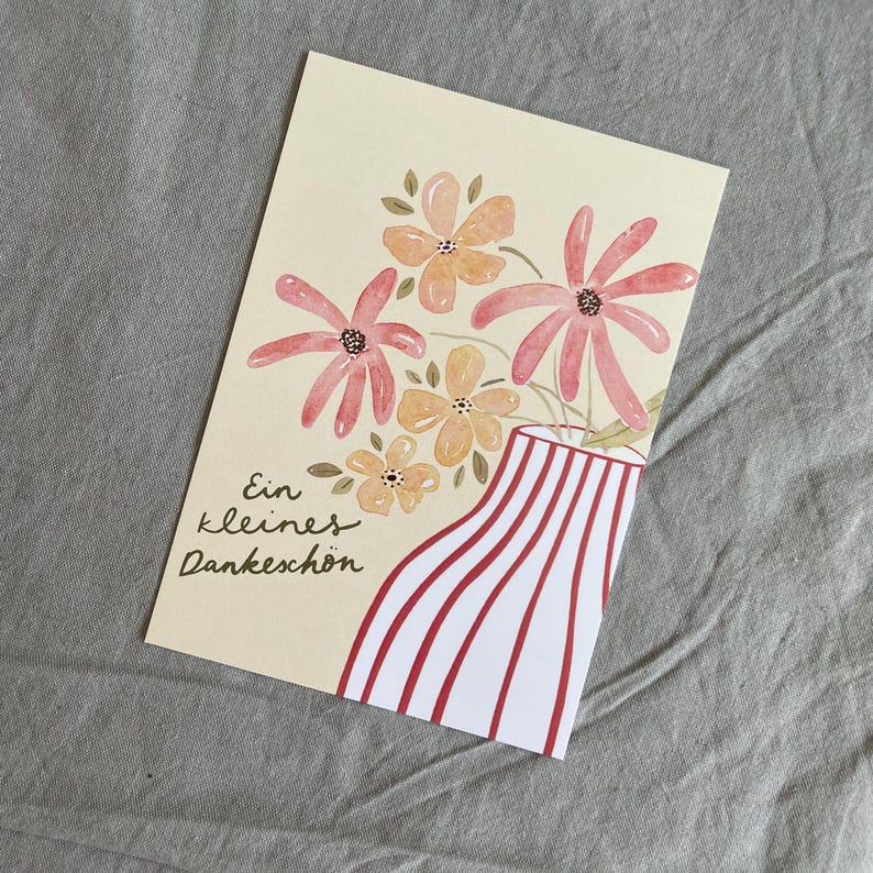 May include: A cream-coloured greeting card with a floral design. The card shows a watercolour illustration of pink and orange flowers in a vase with red and white stripes. The text "Ein kleines Dankesch&ouml;n" is written in black script.