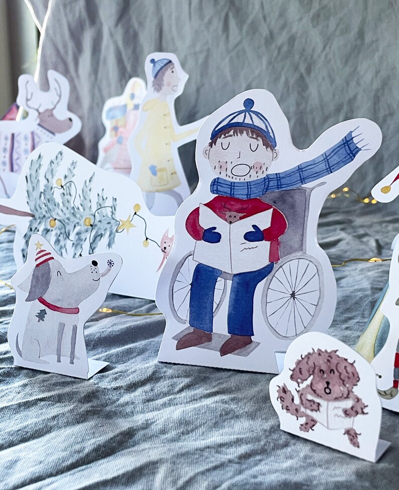 May include: A set of paper Christmas characters, including a person in a wheelchair singing carols, a dog, a tree, and a person wearing a yellow coat. The characters are cut out and ready to be assembled.