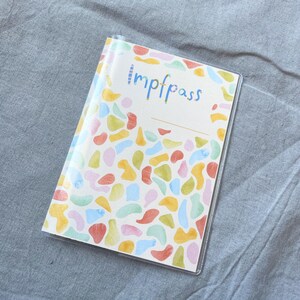 May include: A clear plastic cover with a colorful abstract pattern and the word "Impfpass" printed on the front.