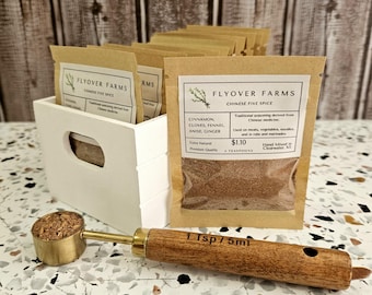 Könnte beinhalten: Ein kleines braunes Papierpäckchen mit einer Mischung aus fünf chinesischen Gewürzen von Flyover Farms. Das Päckchen enthält 1 Teelöffel Zimt, Nelken, Fenchel, Anis und Ingwer. Das Päckchen ist mit den Zutaten, dem Preis und den Gebrauchsanweisungen versehen. Ein kleiner Holzlöffel mit einer Messingspitze ist im Lieferumfang enthalten.