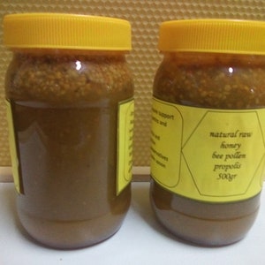 May include: Two glass jars with yellow lids filled with a dark brown honey-like substance. The jars have yellow labels with black text that reads "natural raw honey bee pollen propolis 500gr".