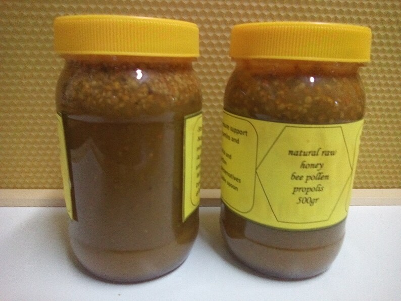May include: Two glass jars with yellow lids filled with a dark brown honey-like substance. The jars have yellow labels with black text that reads "natural raw honey bee pollen propolis 500gr".