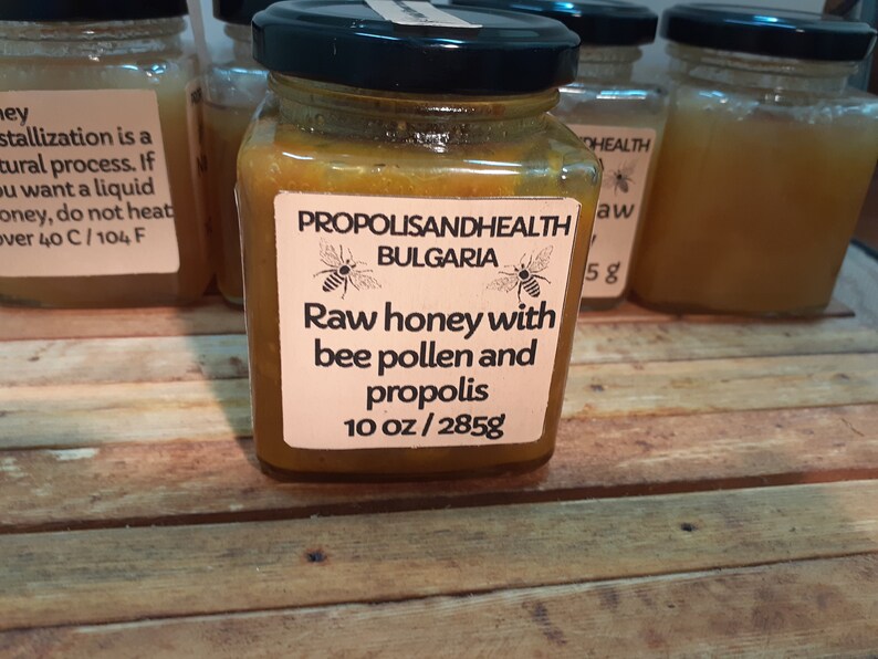 May include: A glass jar of raw honey with bee pollen and propolis from Bulgaria. The label reads "Propolis and Health Bulgaria" with a bee illustration. The jar contains 10 ounces or 285 grams of honey.