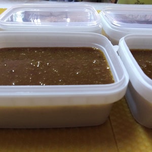 May include: Four white plastic containers filled with a dark brown liquid. The containers are on a yellow surface.