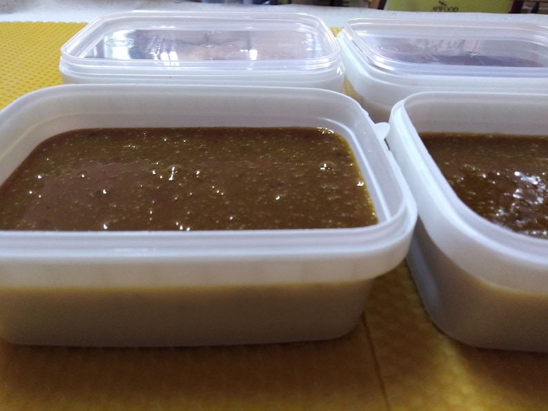 May include: Four white plastic containers filled with a dark brown liquid. The containers are on a yellow surface.