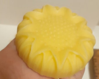 May include: A yellow, round soap bar shaped like a sunflower with a textured center.