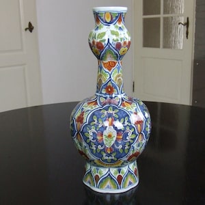 May include: A white ceramic vase with a bulbous body and a long, slender neck. The vase is decorated with a colourful floral pattern in shades of blue, red, yellow, and green.